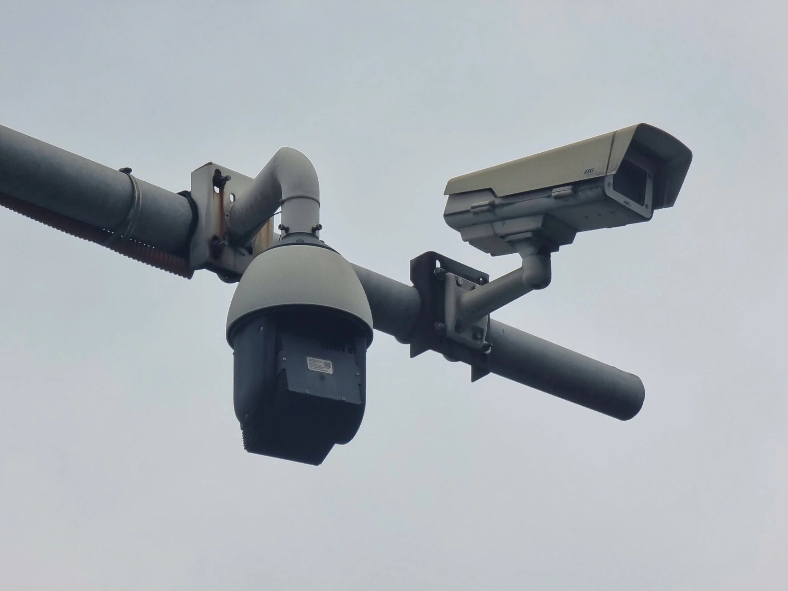 hình ảnh camera phạt nguội gồm hai camera giám sát giao thông gắn trên trụ ngoài trời với nền trời xám