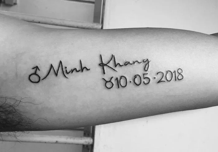 Hình xăm tên Minh Khang kèm ngày tháng năm sinh trên bắp tay
